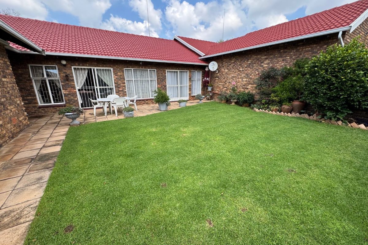 A private rear courtyard featuring a well-maintained lawn, paved patio area, and face brick townhouse exterior with red tiled roofing.