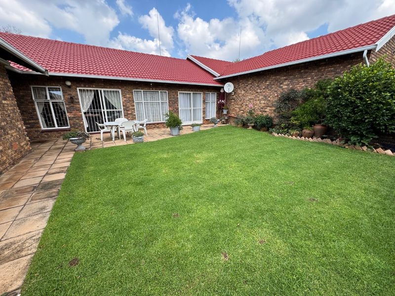 A private rear courtyard featuring a well-maintained lawn, paved patio area, and face brick townhouse exterior with red tiled roofing.