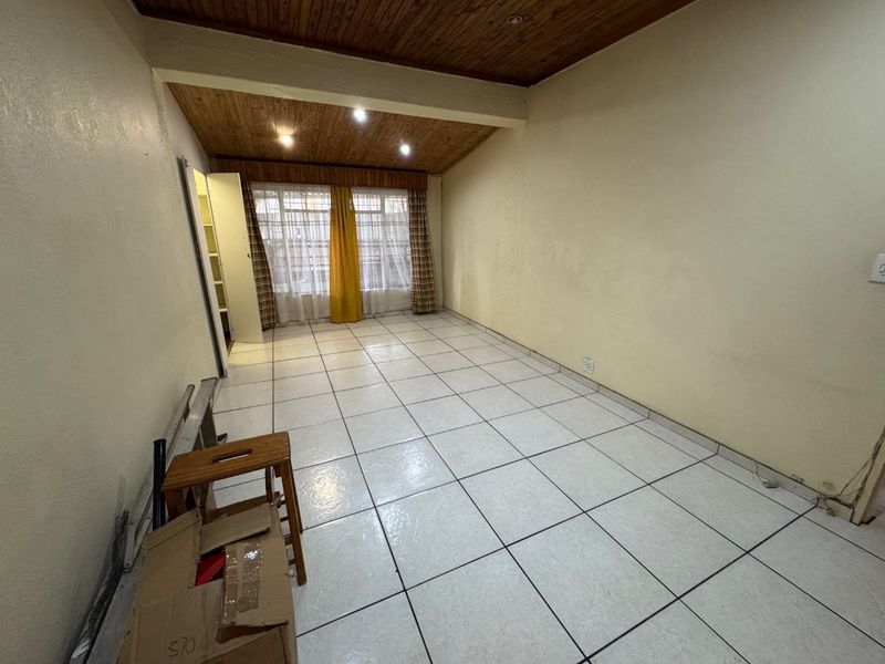 An empty living room featuring tiled flooring and a timber tongue and groove ceiling with recessed lighting.