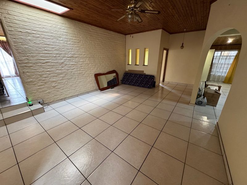 Spacious living area featuring a timber-clad ceiling with a skylight, exposed brick wall, and ceramic tiled flooring, offering a versatile open-plan layout.