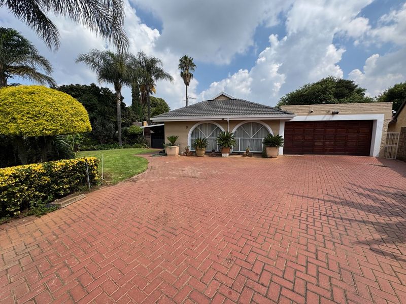 Front view of a single-story house featuring a paved brick driveway, double garage, and distinctive arched windows set within a landscaped garden.