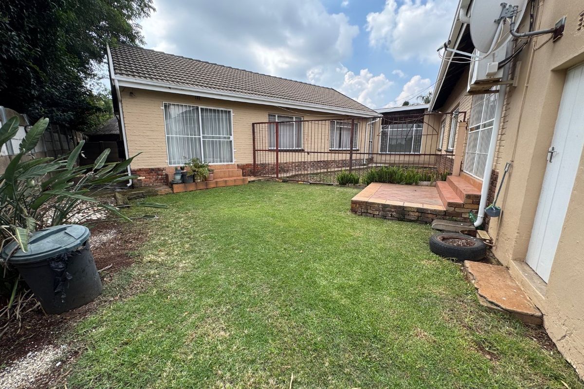 Rear view of the house featuring a lawn, raised patio area, and brick facade with security fencing.