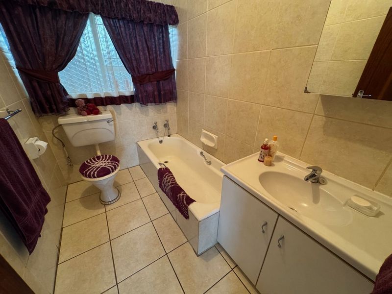 A functional bathroom featuring a built-in vanity, bathtub, and toilet with neutral wall and floor tiling.