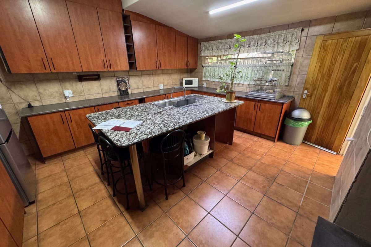Spacious kitchen featuring wooden cabinetry, granite countertops, a central island with a double sink, and tiled flooring throughout.