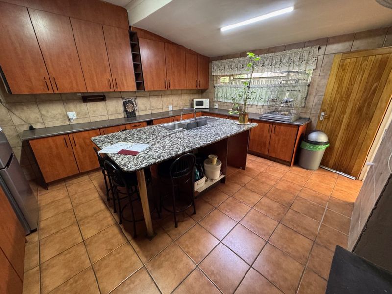 Spacious kitchen featuring wooden cabinetry, granite countertops, a central island with a double sink, and tiled flooring throughout.