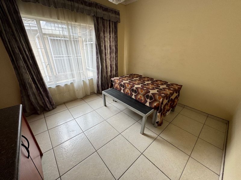 A functional dining area featuring tiled flooring and large windows fitted with security bars, offering a simple and practical space.