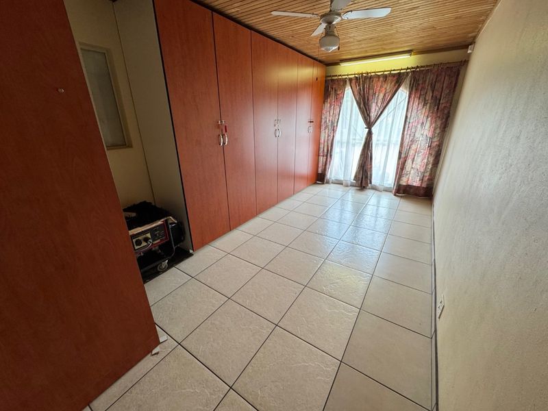 A bedroom featuring built-in cupboards, tiled flooring, and a timber ceiling with a central fan.
