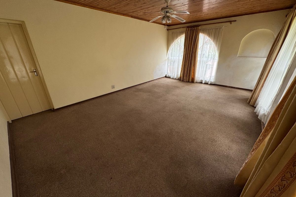 An empty living room featuring a timber-clad ceiling, ceiling fan, and arched windows, requiring cosmetic updates to the walls and flooring.