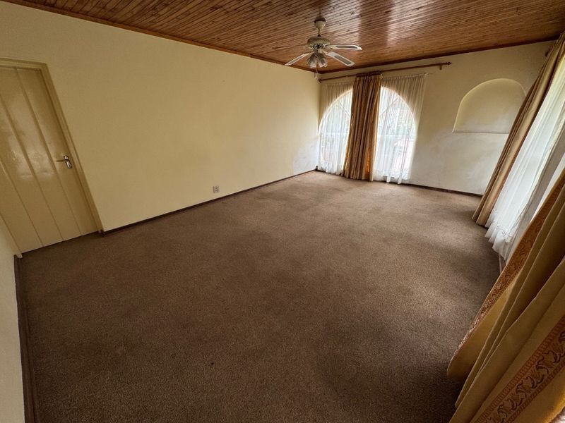 An empty living room featuring a timber-clad ceiling, ceiling fan, and arched windows, requiring cosmetic updates to the walls and flooring.