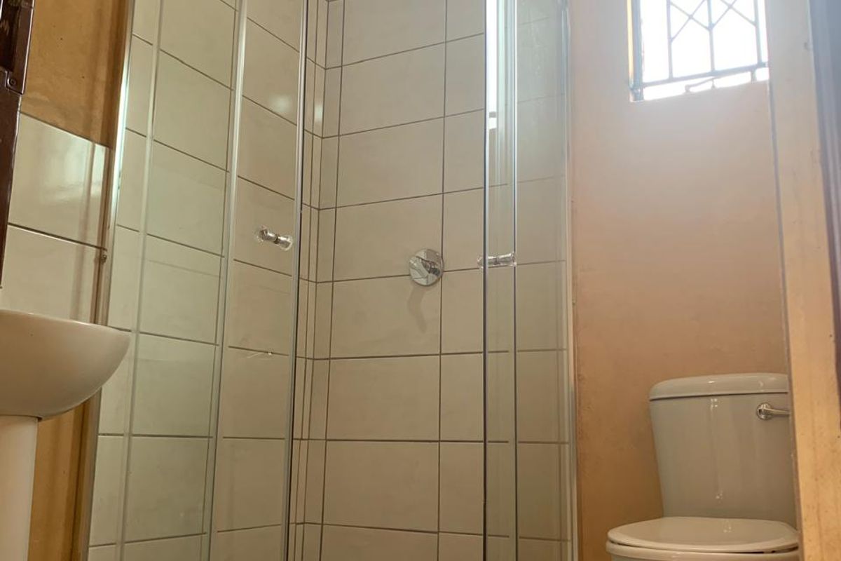 A compact bathroom featuring a glass shower enclosure, pedestal basin, and toilet, requiring cosmetic updates to wall finishes and flooring.
