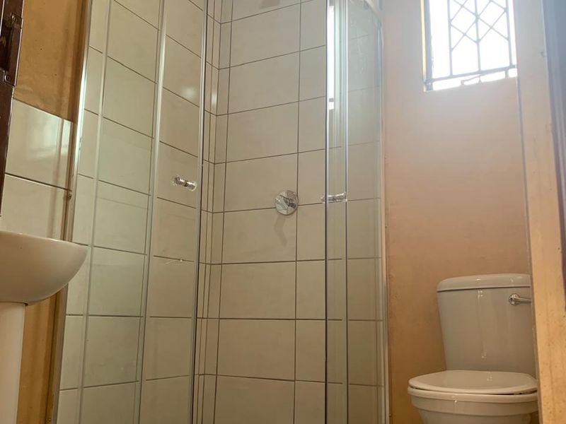 A compact bathroom featuring a glass shower enclosure, pedestal basin, and toilet, requiring cosmetic updates to wall finishes and flooring.