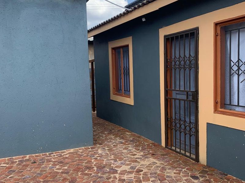 A view of the rear exterior area featuring cobblestone paving, security gates, and well-maintained painted walls.