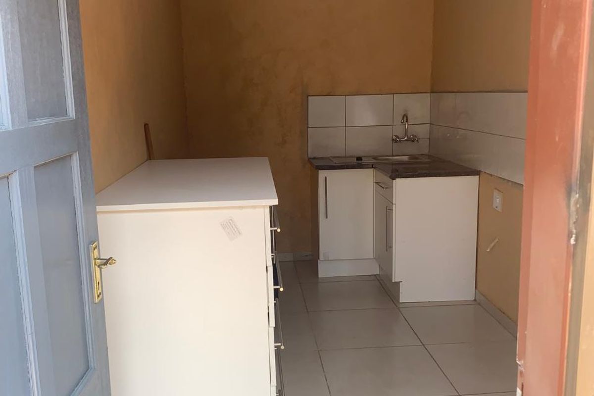 A compact kitchen area featuring basic base cabinetry, a sink with a tiled backsplash, and neutral floor tiling.