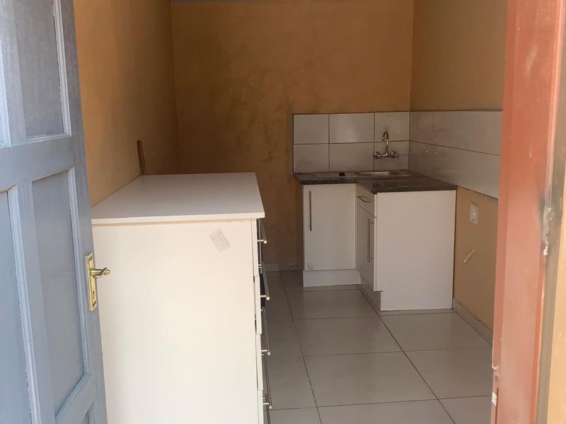 A compact kitchen area featuring basic base cabinetry, a sink with a tiled backsplash, and neutral floor tiling.