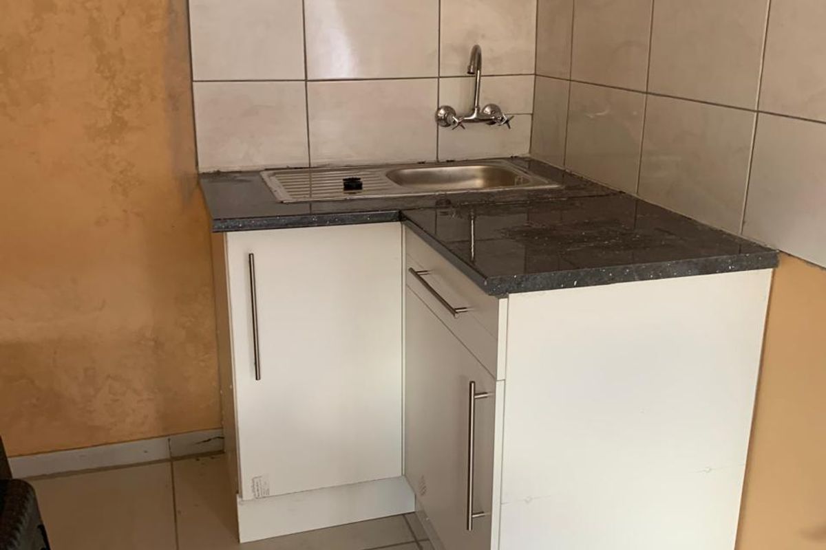A compact kitchenette featuring a stainless steel sink, tiled backsplash, and basic white base cabinetry with a dark countertop.