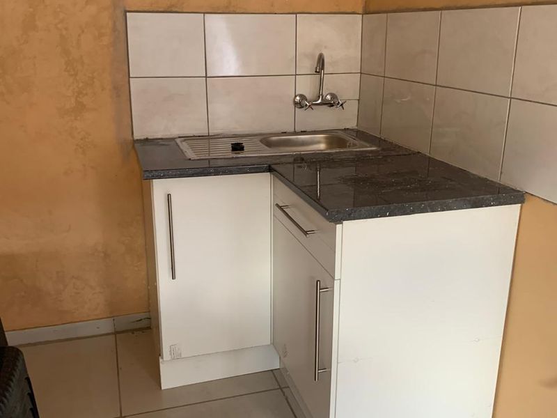 A compact kitchenette featuring a stainless steel sink, tiled backsplash, and basic white base cabinetry with a dark countertop.