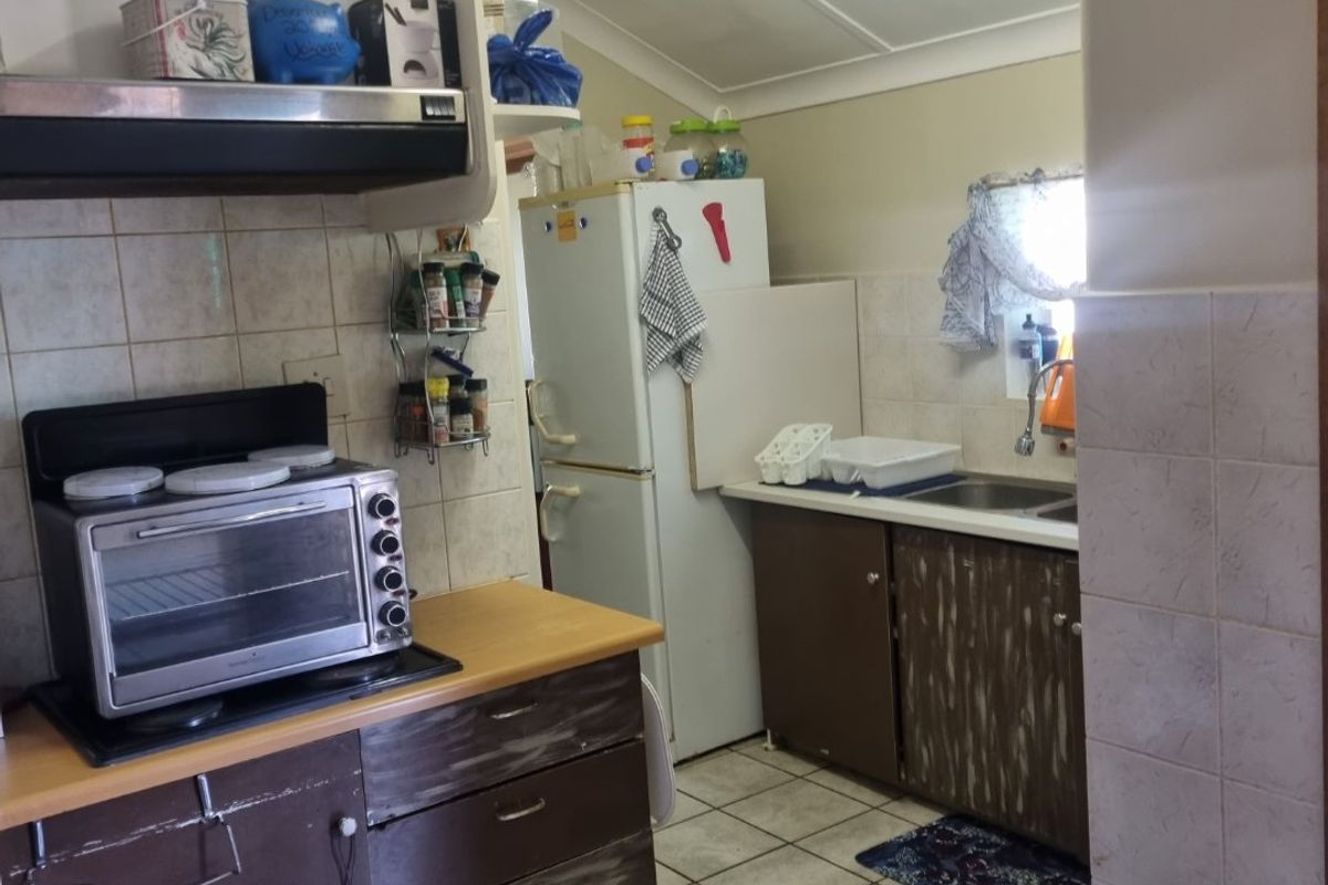 A functional kitchen featuring tiled flooring, built-in cabinetry, a sink, and an extractor fan, with a sloped ceiling and tiled splashbacks.