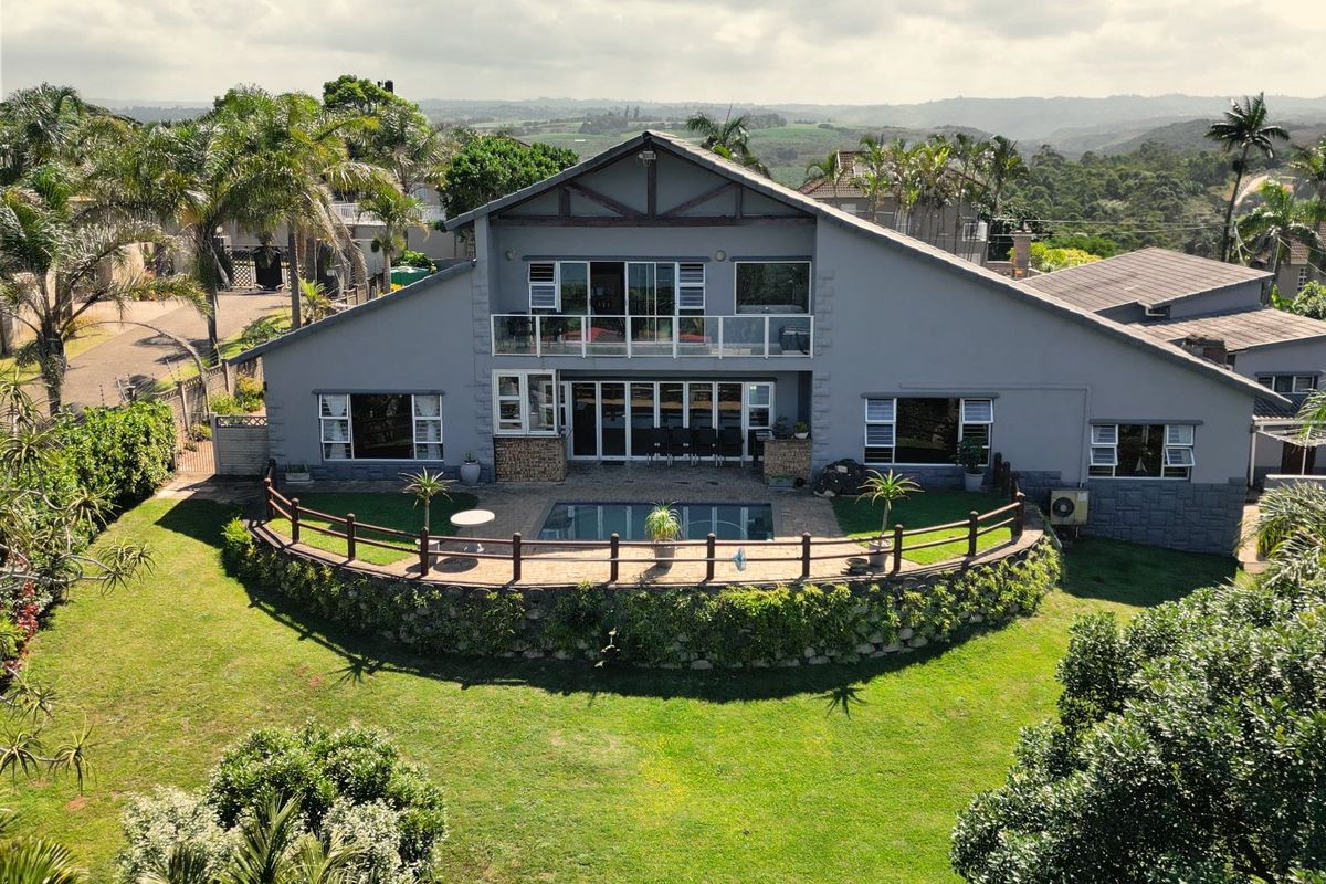 Aerial view of a two-story residential property featuring a swimming pool, paved patio area, and a balcony overlooking a landscaped garden.