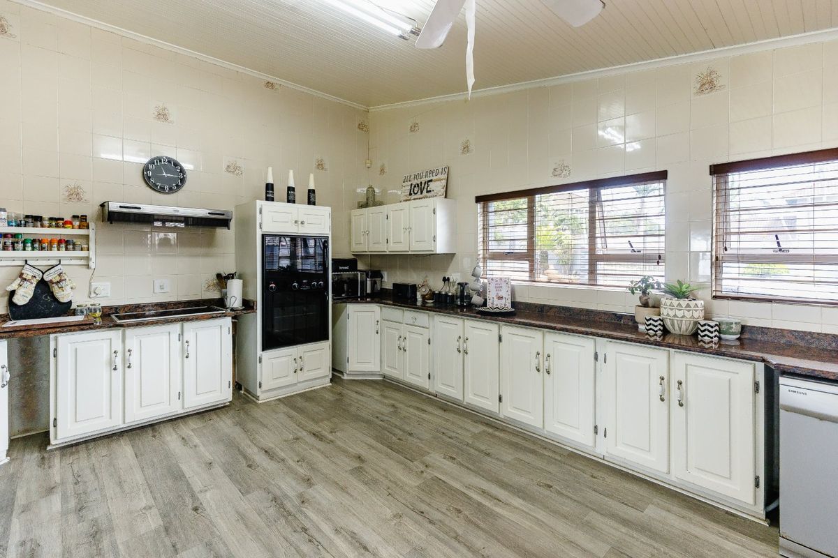 A functional kitchen featuring white cabinetry, granite countertops, built-in oven, extractor fan, and tiled splashbacks with durable laminate flooring.