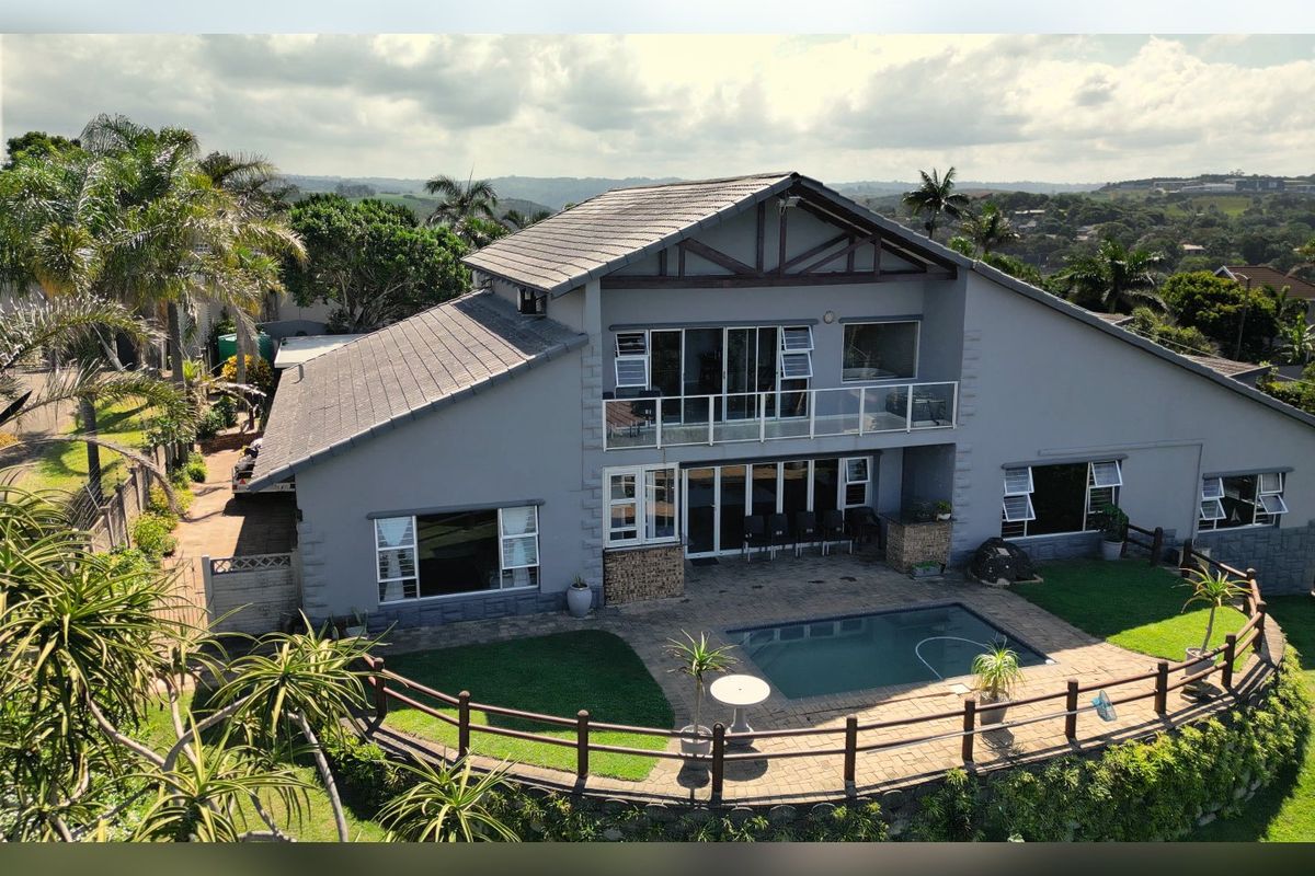 Aerial view of the rear elevation featuring a swimming pool, paved patio area, upper-level balcony, and landscaped garden with scenic views.