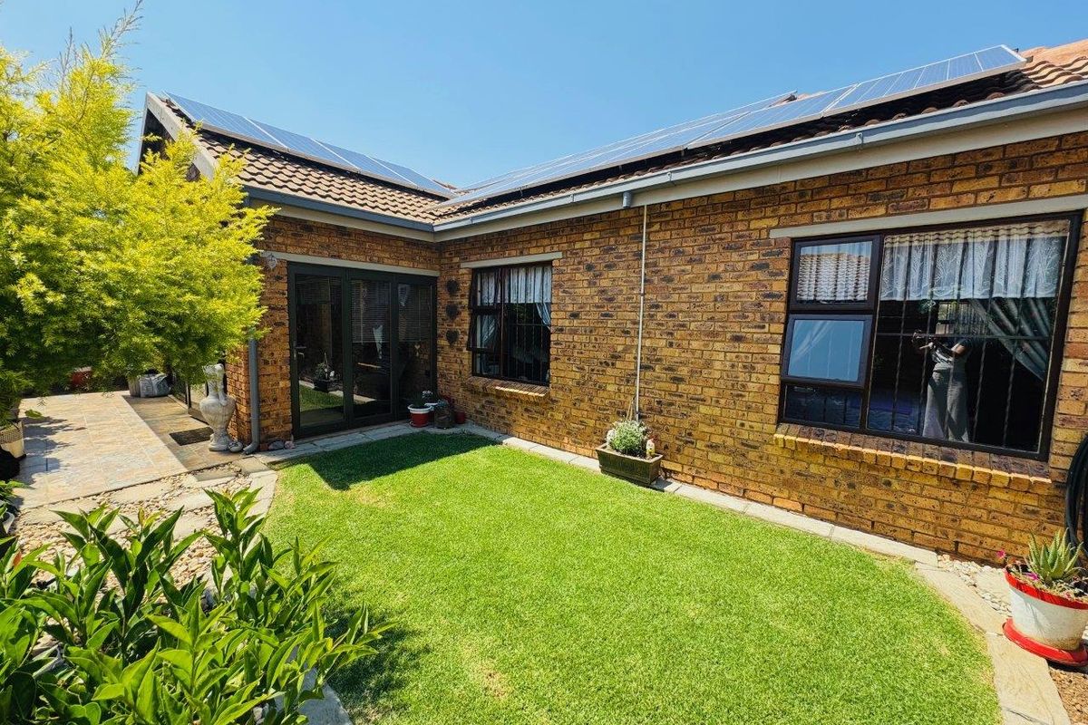 Rear view of the townhouse featuring a face brick facade, solar panels on the tiled roof, a small lawn, and paved outdoor area.