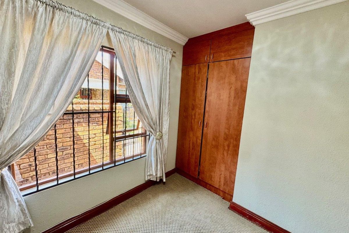 A compact bedroom featuring built-in wooden cabinetry, carpeted flooring, and a window fitted with security bars.