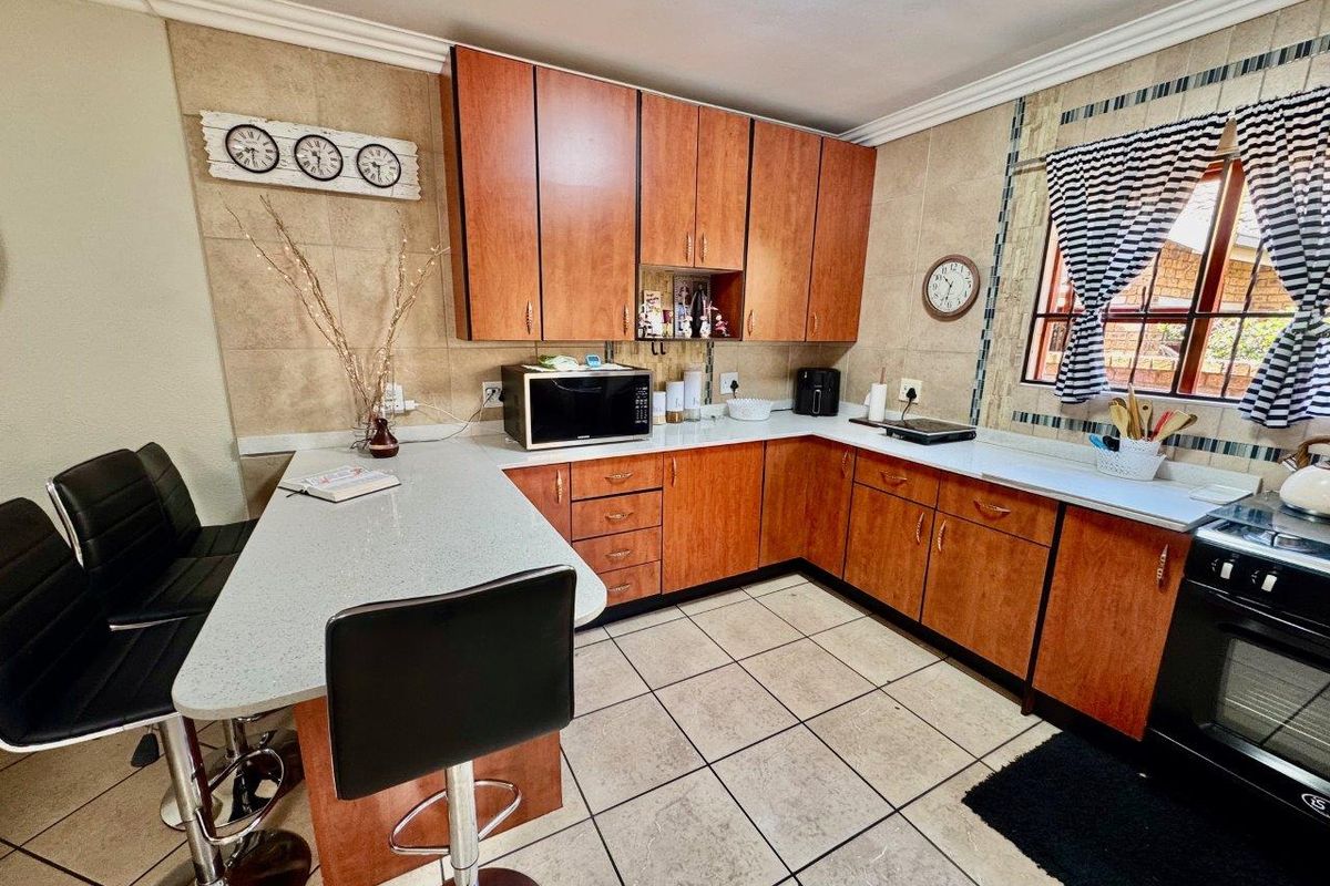 Functional kitchen featuring wood-finish cabinetry, stone-look countertops, a breakfast bar, and tiled flooring with a built-in oven and hob.