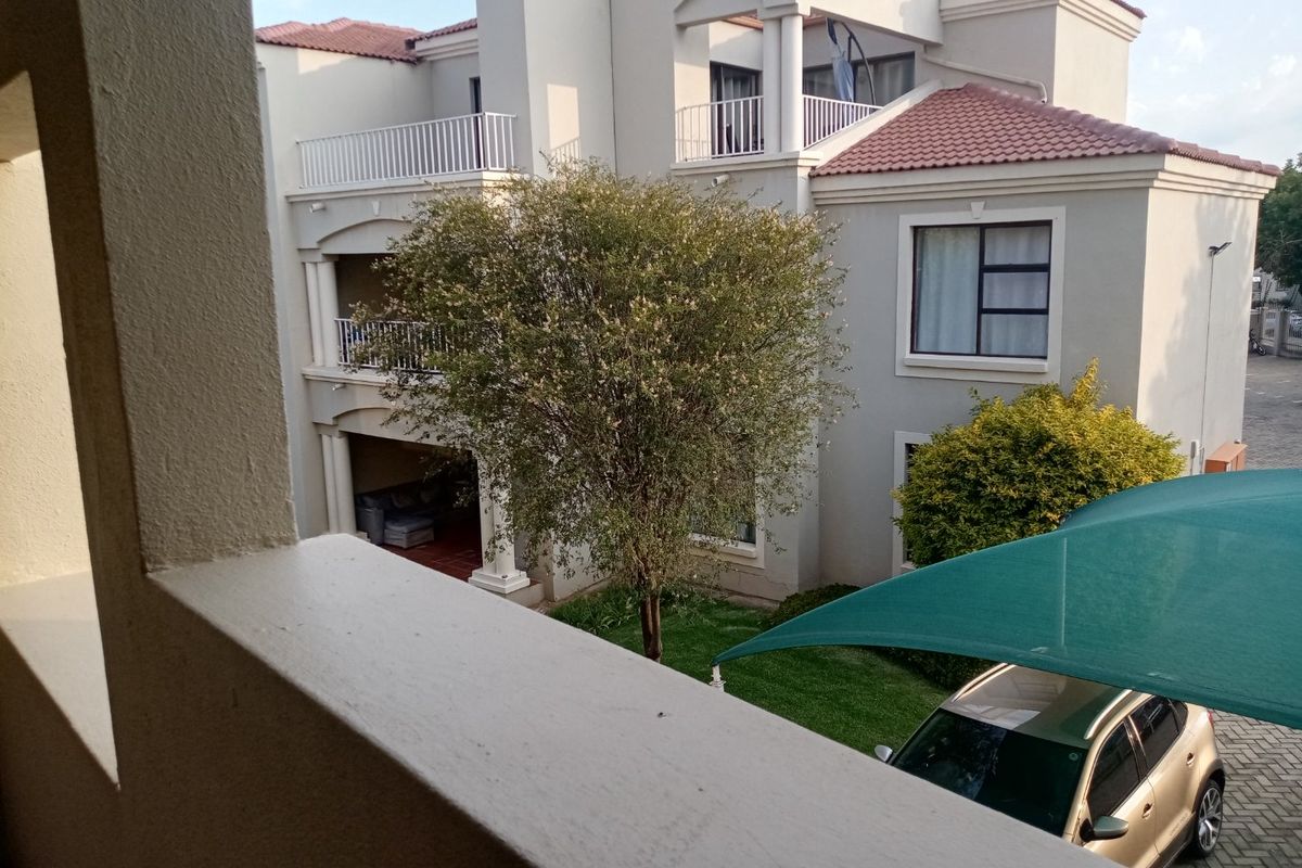 View of the rear building elevation featuring balconies, tiled roofing, and a paved driveway area with a shade sail.