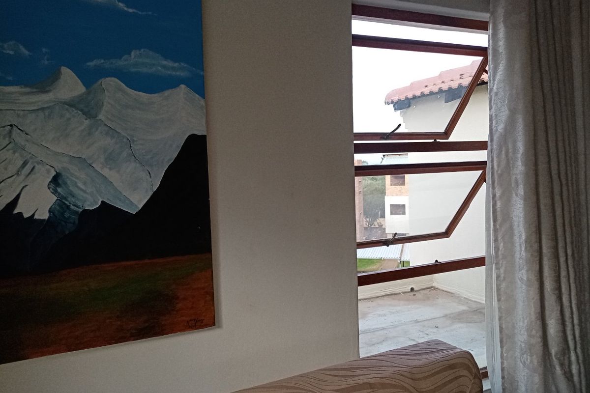 A bedroom interior featuring a timber-framed top-hung window with views of the surrounding apartment complex.