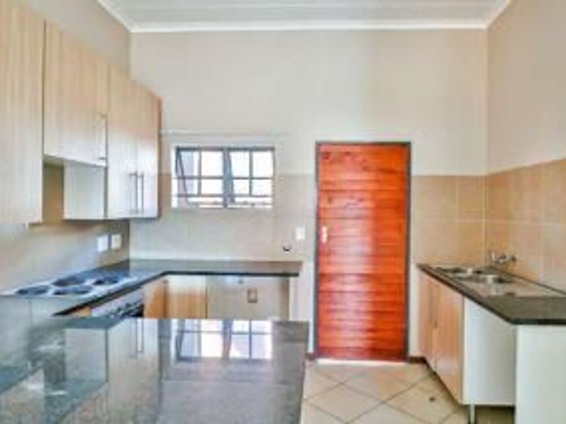 A functional kitchen featuring light wood cabinetry, granite countertops, an electric hob, and a double basin sink with tiled splashbacks.
