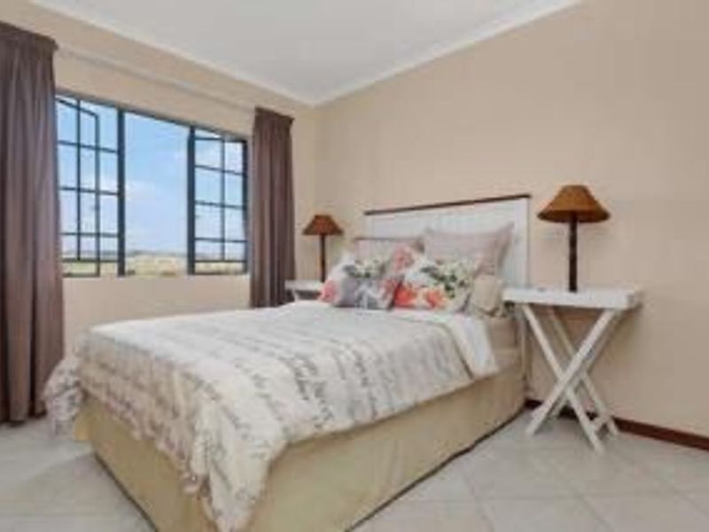 A well-lit bedroom featuring tiled flooring, neutral wall finishes, and large casement windows that provide natural light and exterior views.