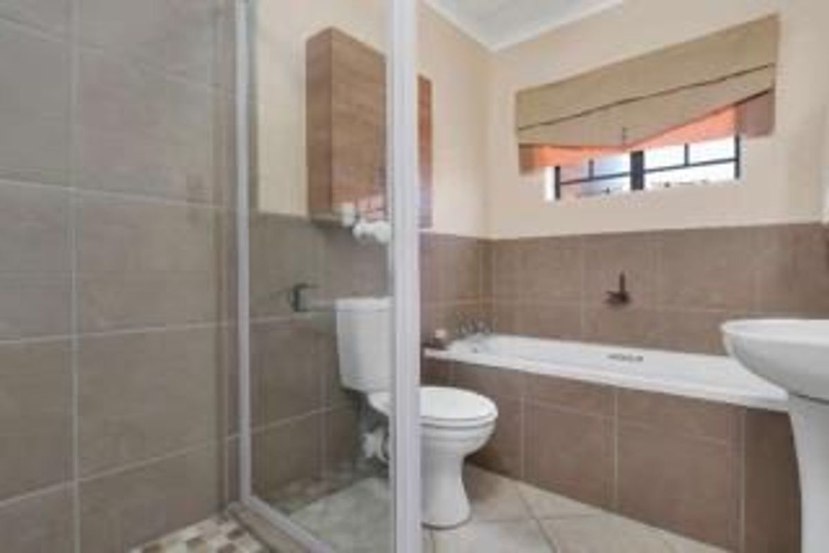 A functional bathroom featuring a shower enclosure, bathtub, pedestal basin, and toilet with neutral wall tiling and tiled flooring.