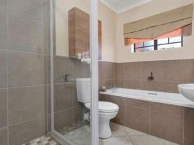 A functional bathroom featuring a shower enclosure, bathtub, pedestal basin, and toilet with neutral wall tiling and tiled flooring.