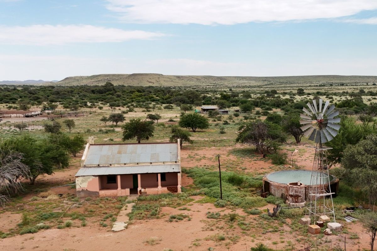 Aerial view of a rural farmstead featuring a traditional farmhouse, a functional windmill, and a circular water reservoir set within an expansive landscape.