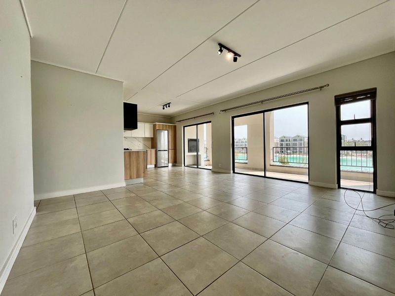 Spacious open-plan living area featuring tiled floors, modern kitchen cabinetry, and large sliding doors leading to a balcony with outdoor views.