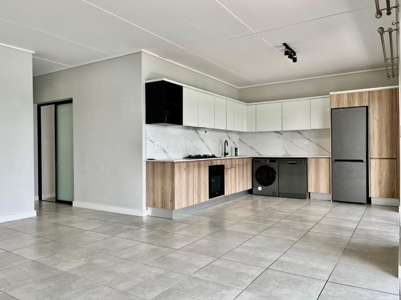 Modern open-plan kitchen featuring sleek two-tone cabinetry, marble-look splashback, integrated appliances, and neutral tiled flooring in a well-maintained apartment setting.