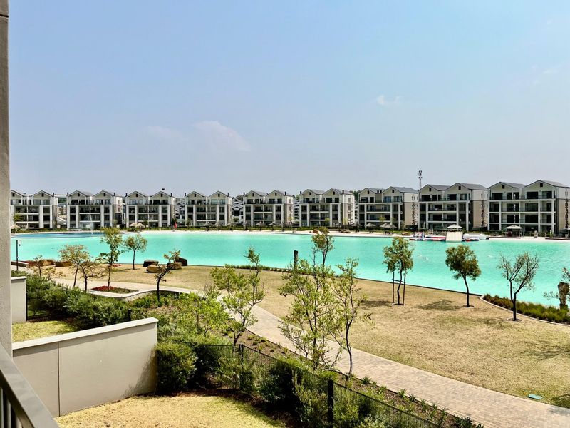 A scenic view overlooking a large turquoise man-made lagoon, landscaped gardens, and modern apartment blocks in a well-maintained residential estate.
