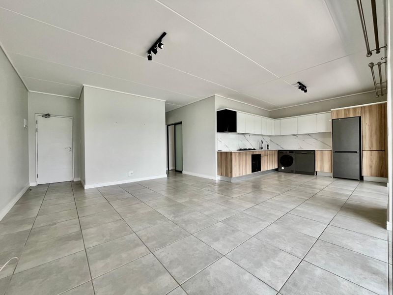 Spacious open-plan living area featuring modern tiled floors, track lighting, and a contemporary kitchen with sleek cabinetry and integrated appliances.