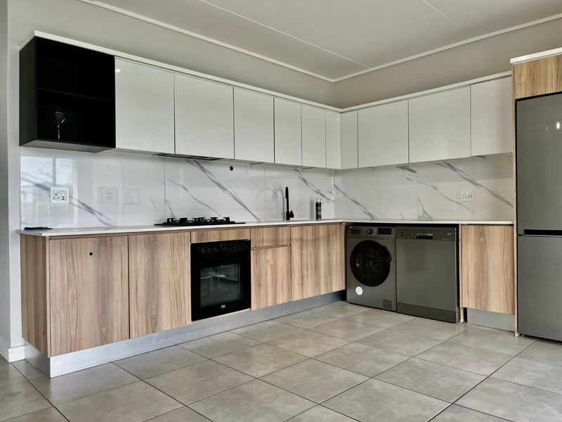 Modern kitchen featuring sleek white and wood-grain cabinetry, marble-look splashback, integrated oven, gas hob, and tiled flooring in a clean, contemporary layout.