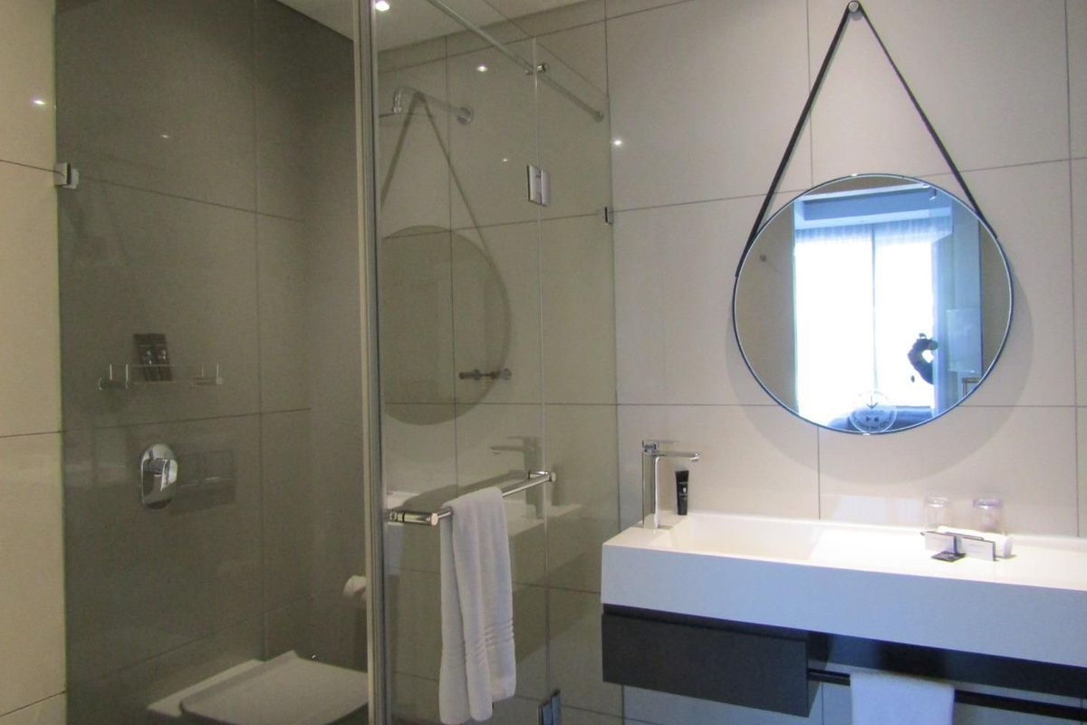 Modern bathroom featuring a sleek wall-mounted vanity, contemporary mixer tap, and a spacious glass-enclosed shower with neutral floor-to-ceiling tiling.