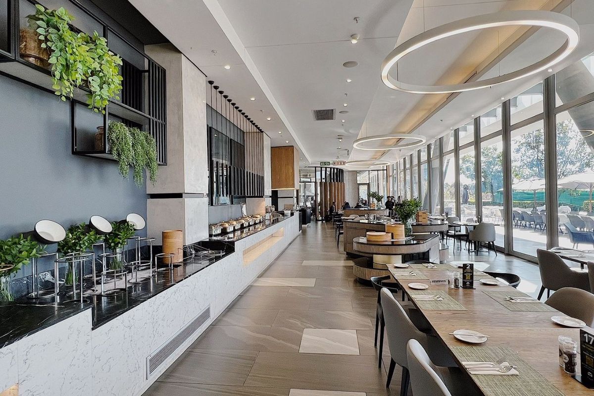 Modern, high-end clubhouse dining area featuring marble buffet counters, large floor-to-ceiling windows, and contemporary circular lighting fixtures.