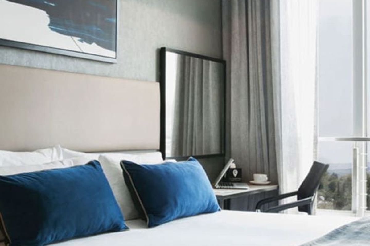 Modern bedroom featuring a neutral color palette, upholstered headboard, sleek pendant lighting, and floor-to-ceiling glass doors leading to an outdoor space.
