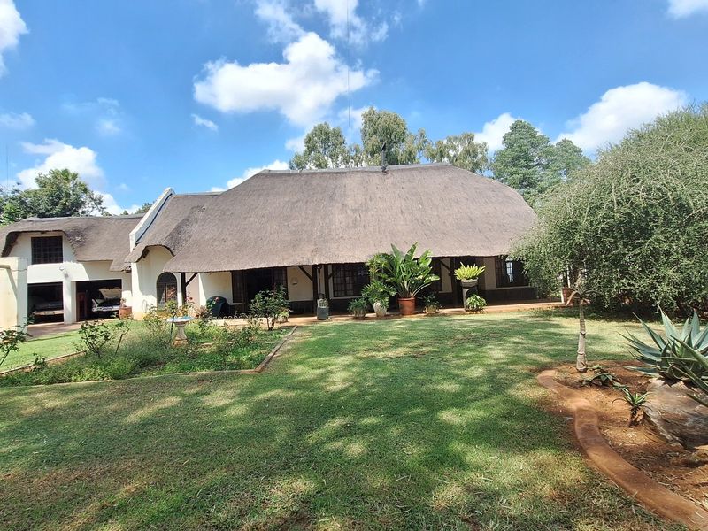 A charming house featuring a traditional thatched roof, a spacious covered patio, and a well-maintained garden with a double garage.
