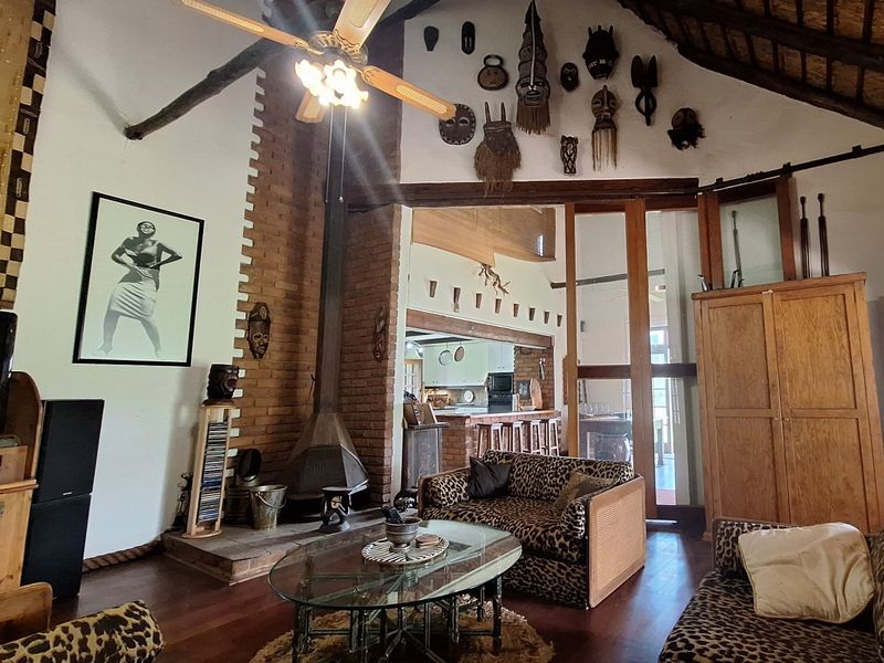 Spacious open-plan living area featuring a high thatched ceiling with exposed beams, a brick fireplace, and timber flooring, connecting to the kitchen area.
