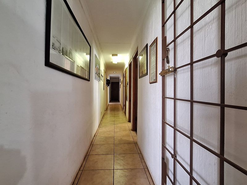 A long residential hallway featuring tiled flooring, a security gate, and multiple doorways leading to other rooms.