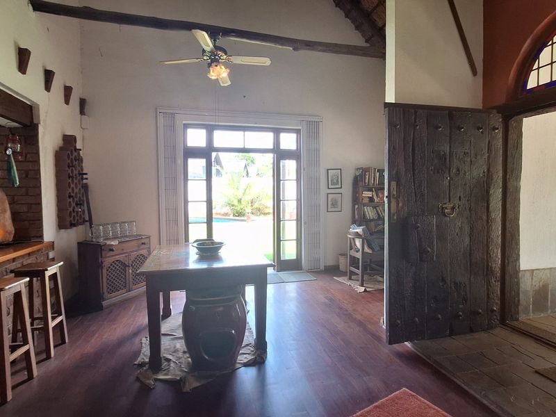 Spacious living area featuring exposed timber beams, rich wood flooring, a rustic brick wall, and direct access to the outdoor patio area.