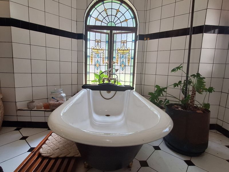 A characterful bathroom featuring a classic freestanding bathtub positioned beneath a decorative stained glass window with traditional black and white tiled finishes.
