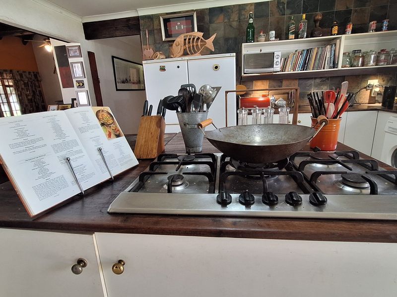 A functional kitchen featuring a central island with a gas cooktop, slate tile backsplash, and built-in cabinetry with a wooden countertop.