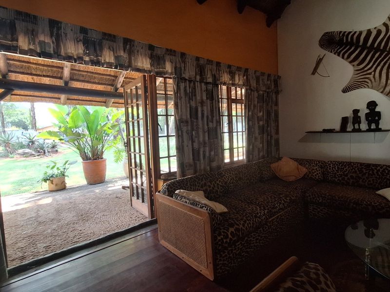 Living room featuring timber flooring, exposed thatch ceiling, and large timber-framed glass doors opening onto a covered patio area.