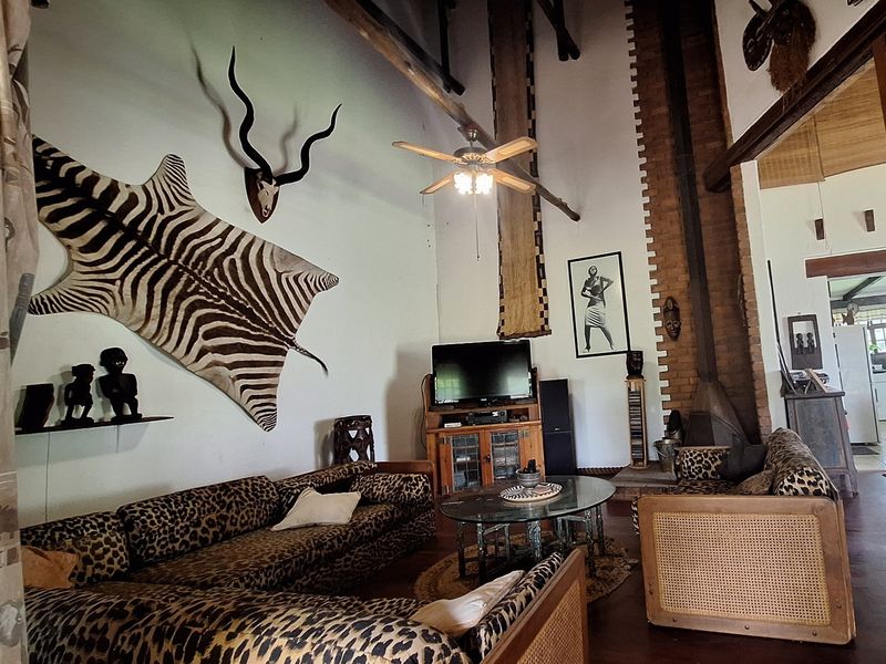 Spacious living room featuring a vaulted ceiling with exposed timber beams, a brick fireplace, and hardwood flooring.